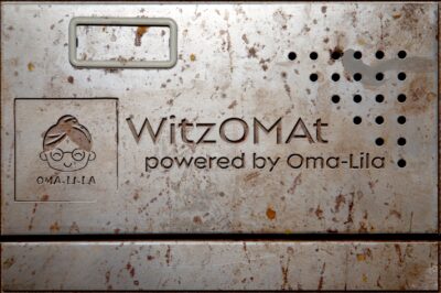 Metallplatte mit eingraviertem Logo und Text des WitzOMat von Oma-Lila.